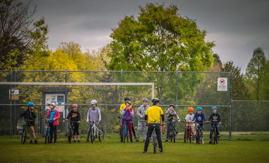 School aged kids lined up on grass field with bikes