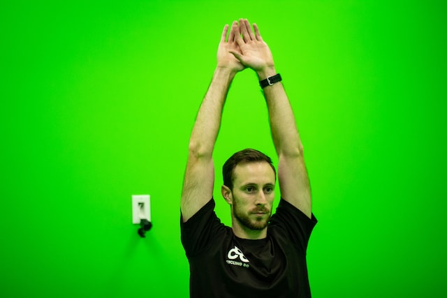 Cycling coach in a motion capture green room reaching above his head.