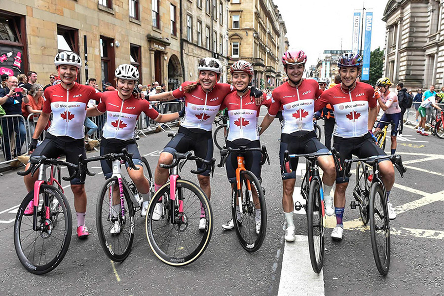 Female cyclists in red and white team Canada jerseys lined up shoulder to shoulder on their bikes.