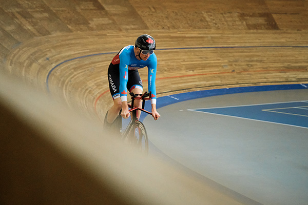 A cyclist in team canada kit on a track bike on a velodrome.