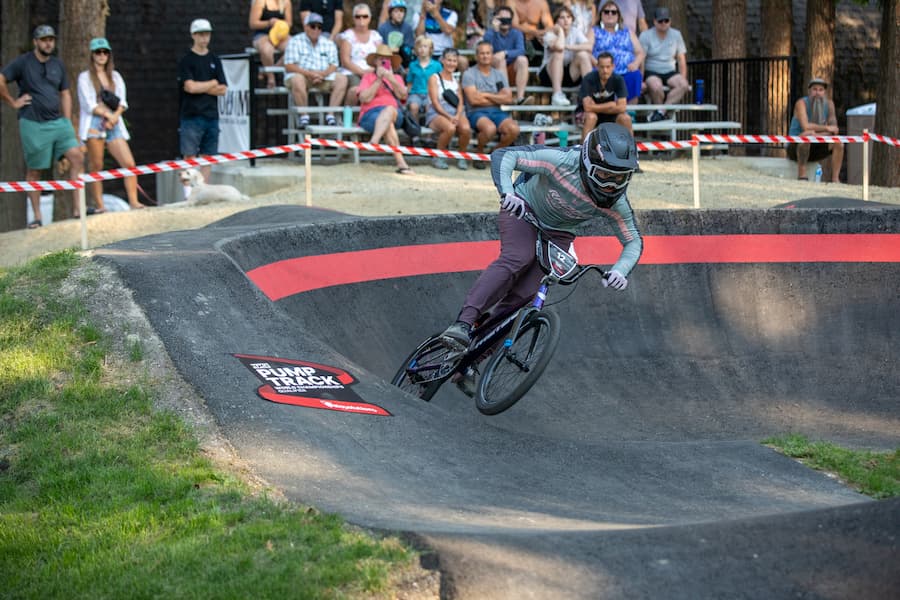 A cyclist riding on a pump track with spectators watching from the bleachers.