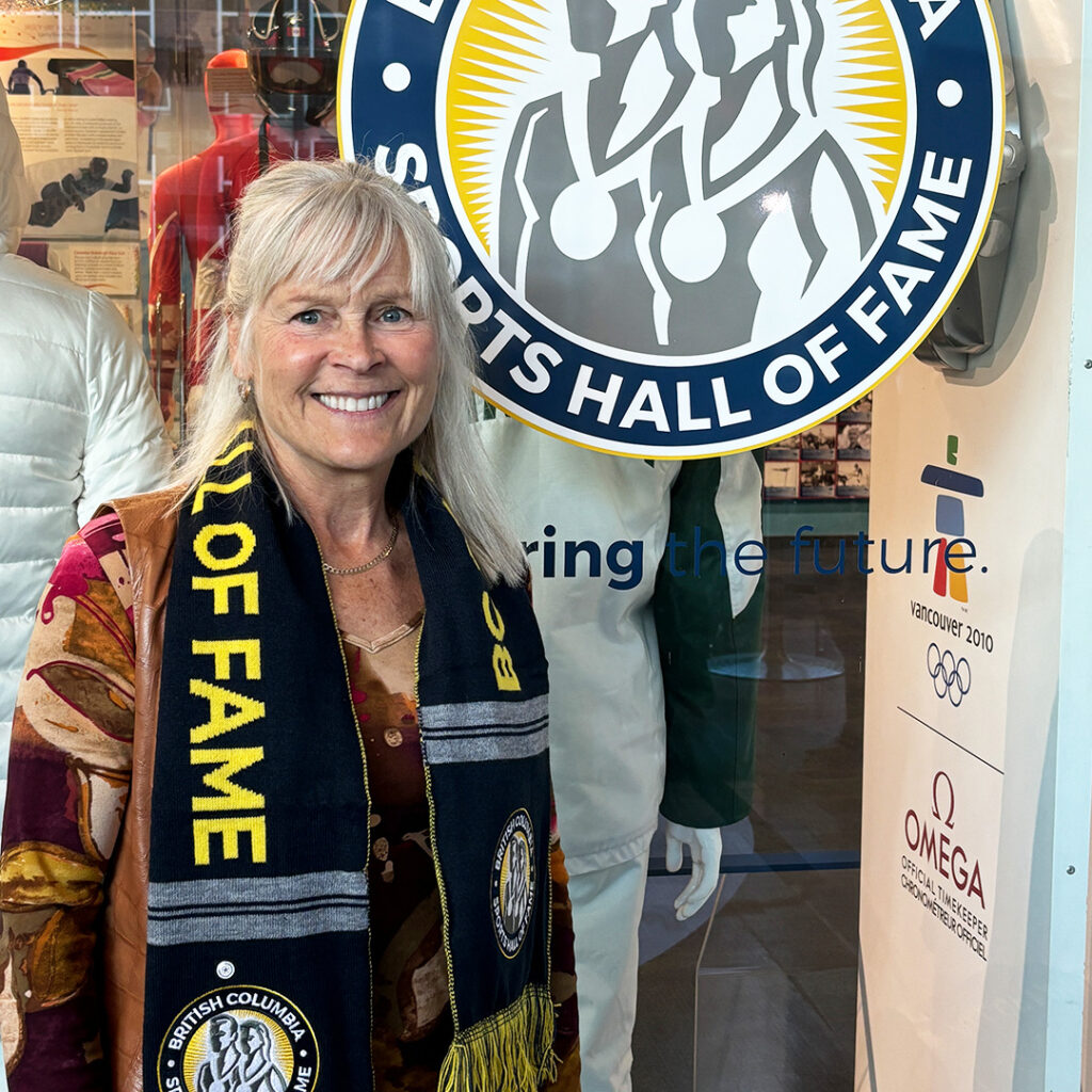 A woman wearing a Hall of Fame scarf smiling beside the BC Sports Hall of Fame logo.