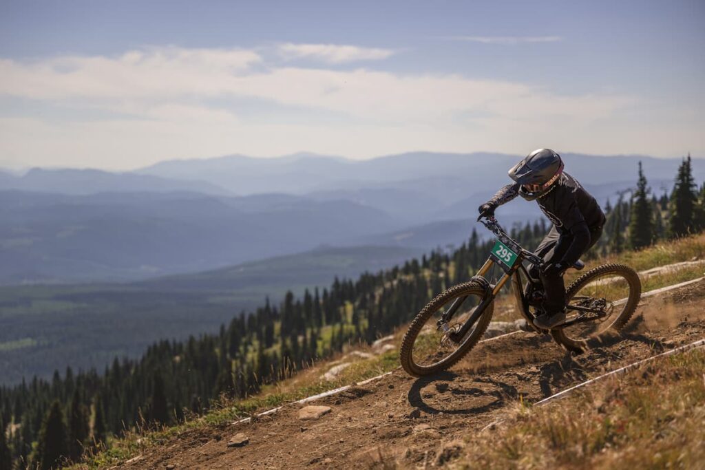 A mountain biker riding down a trail with mountain range backdrop