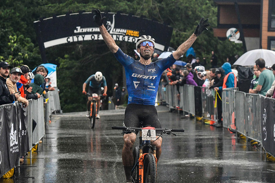 Mountain biker crosses the finish line with arms raised in victory